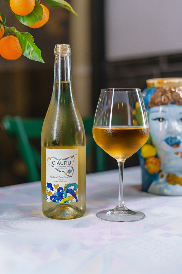 Bottiglia di vino bianco, bicchiere pieno e ramo di arancio su un tavolo.
