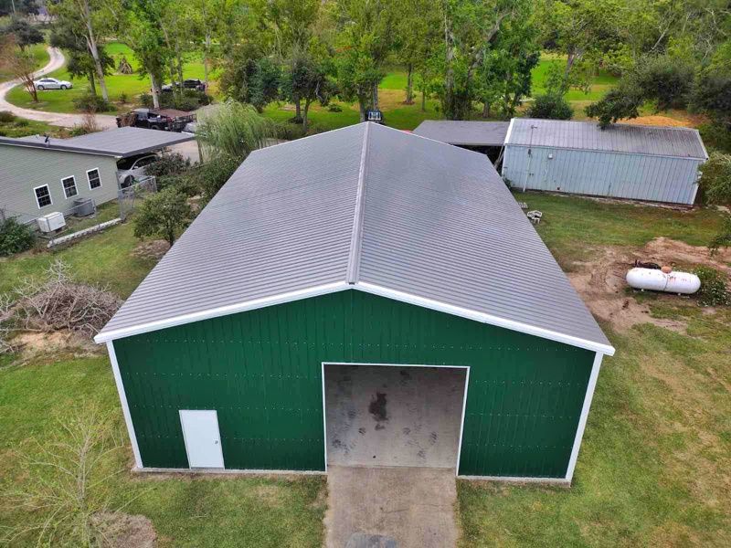 An aerial view of a green and white barn with a gray roof.