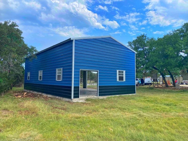A blue and black metal building is sitting in the middle of a grassy field.