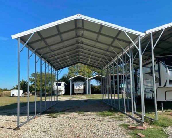 A carport with a white roof is sitting on top of a gravel road.