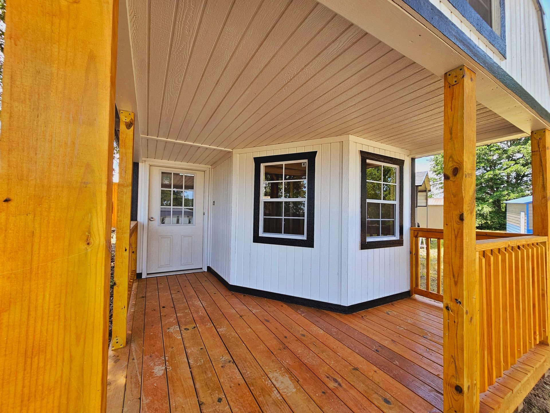 A porch with a wooden deck and a white house in the background.