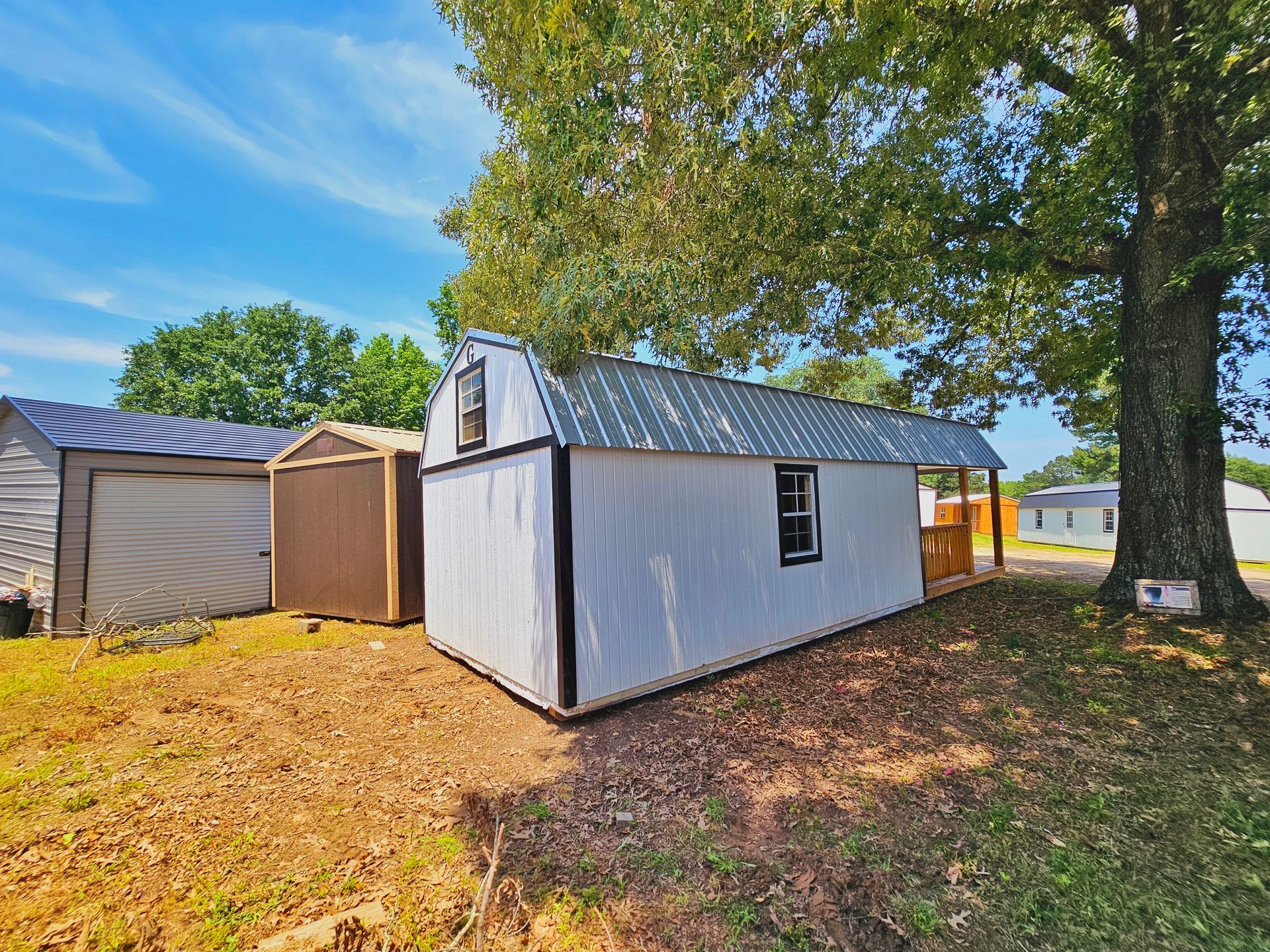 A white barn shed is sitting in the middle of a grassy field next to a garage.
