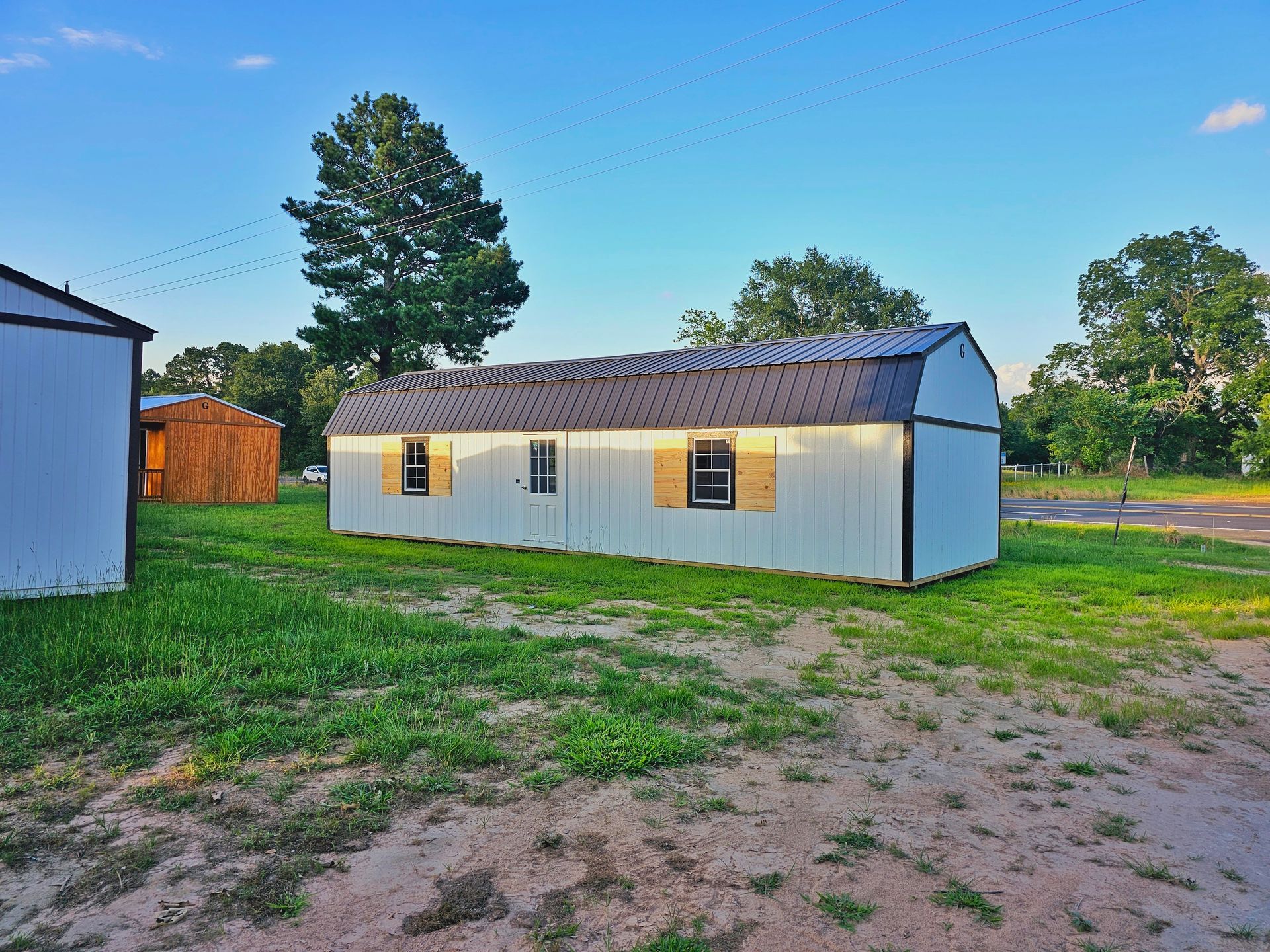 A white shed is sitting in the middle of a grassy field.