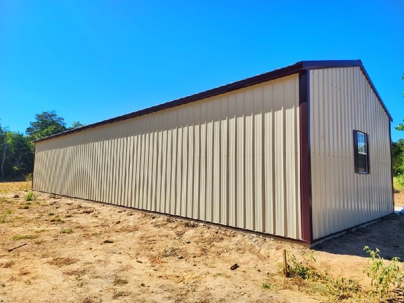 A large metal building is sitting in the middle of a dirt field.