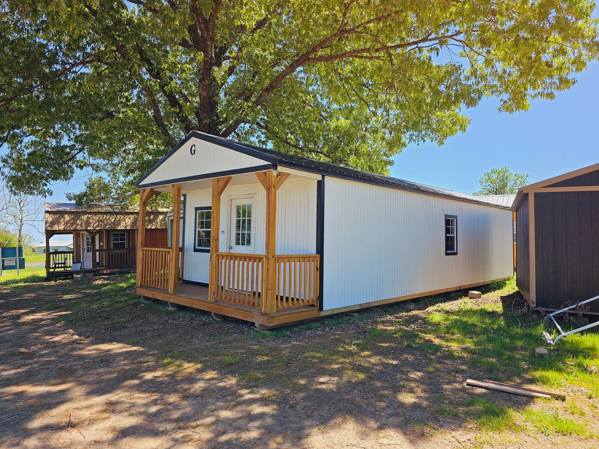 A small white house with a porch and a shed in the background.