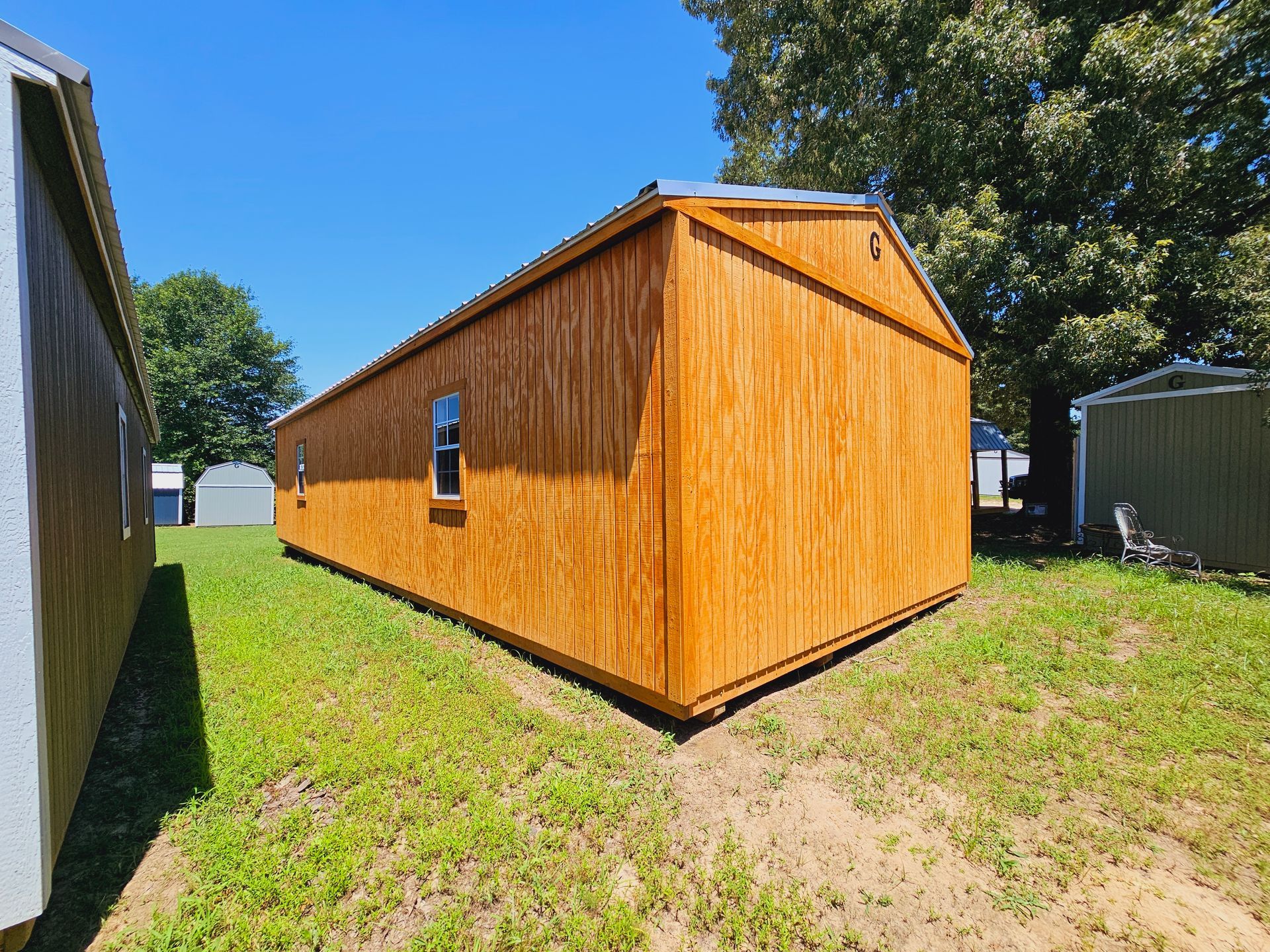 A wooden shed is sitting in the middle of a grassy field.
