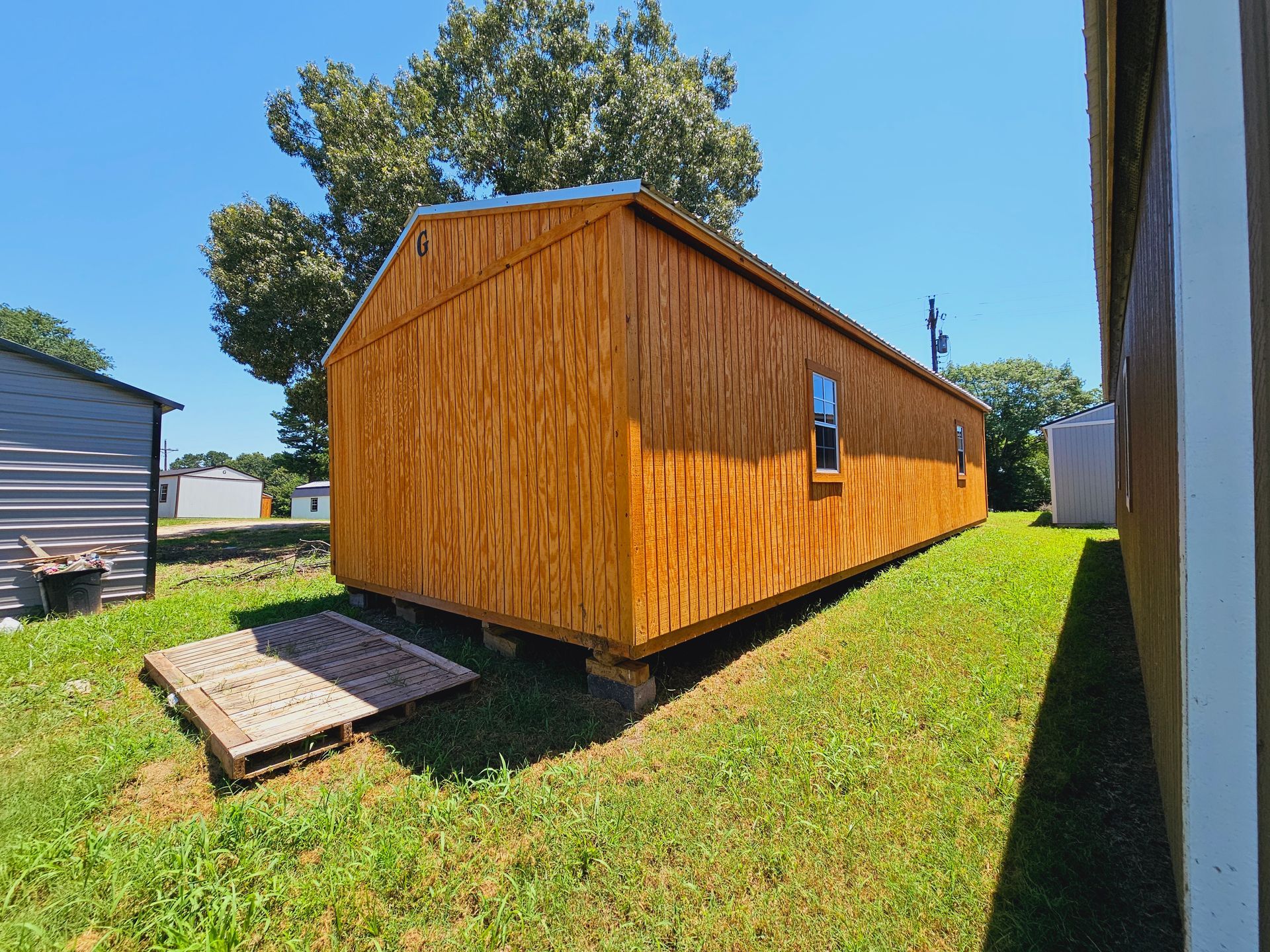 A long wooden shed is sitting in the middle of a lush green field.
