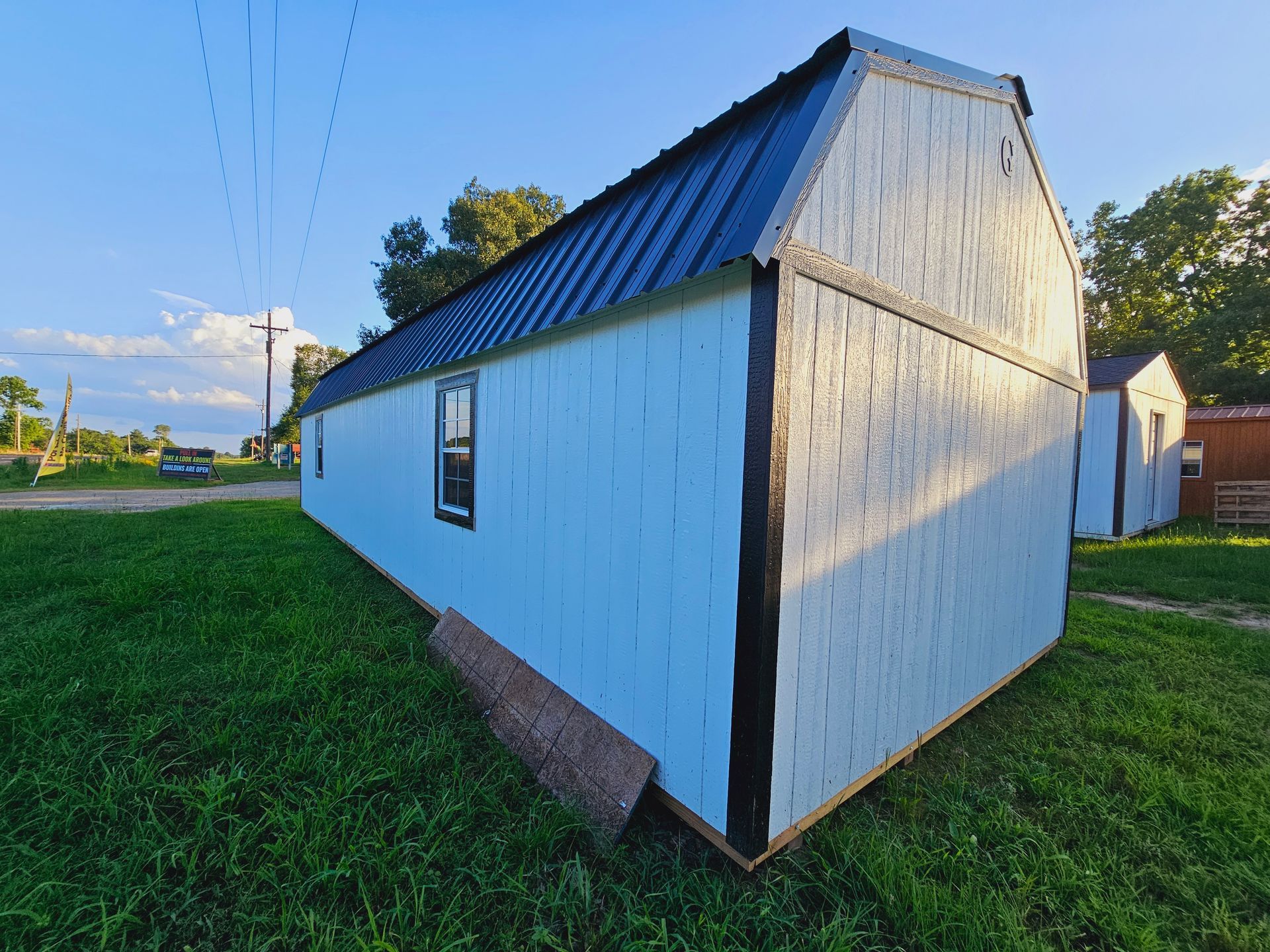 A white building with a black roof is sitting in the middle of a grassy field.