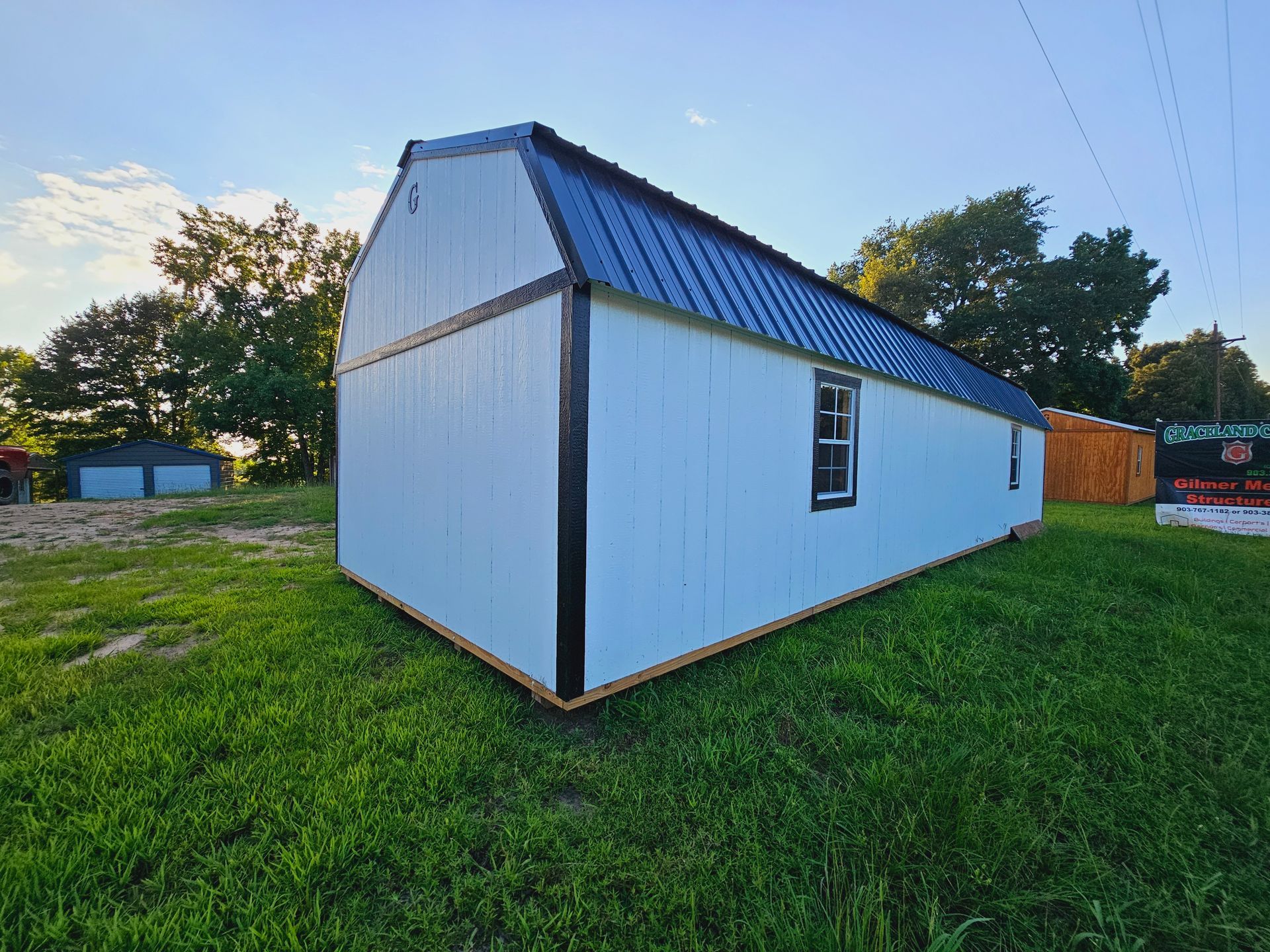 A white barn with a black roof is sitting in the middle of a grassy field.