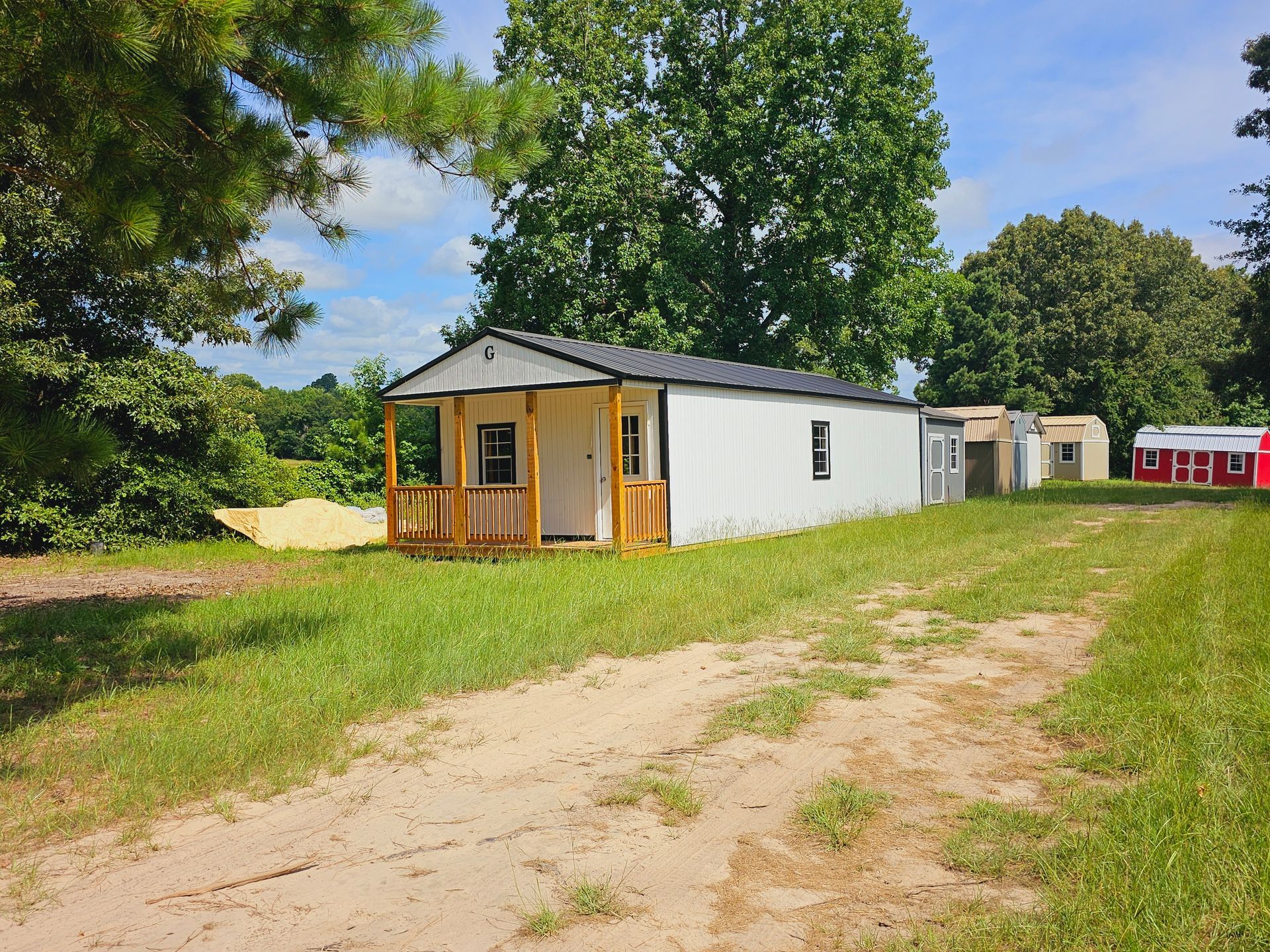 A small white house with a porch is sitting in the middle of a grassy field.