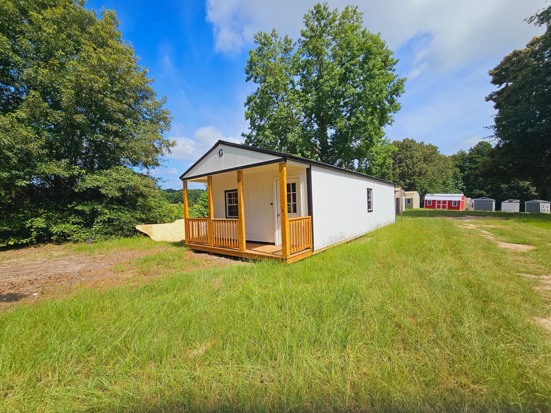 A small white house with a porch is sitting in the middle of a grassy field.