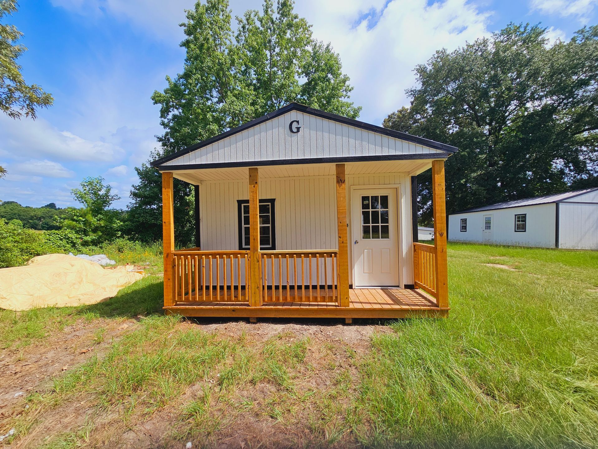A small white house with a porch is sitting in the middle of a grassy field.