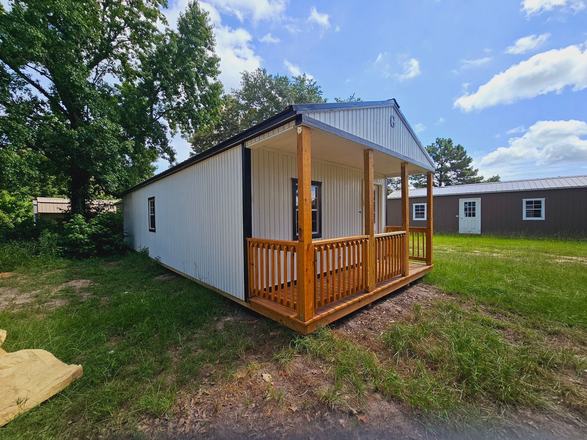 A small house with a porch is sitting on top of a lush green field.