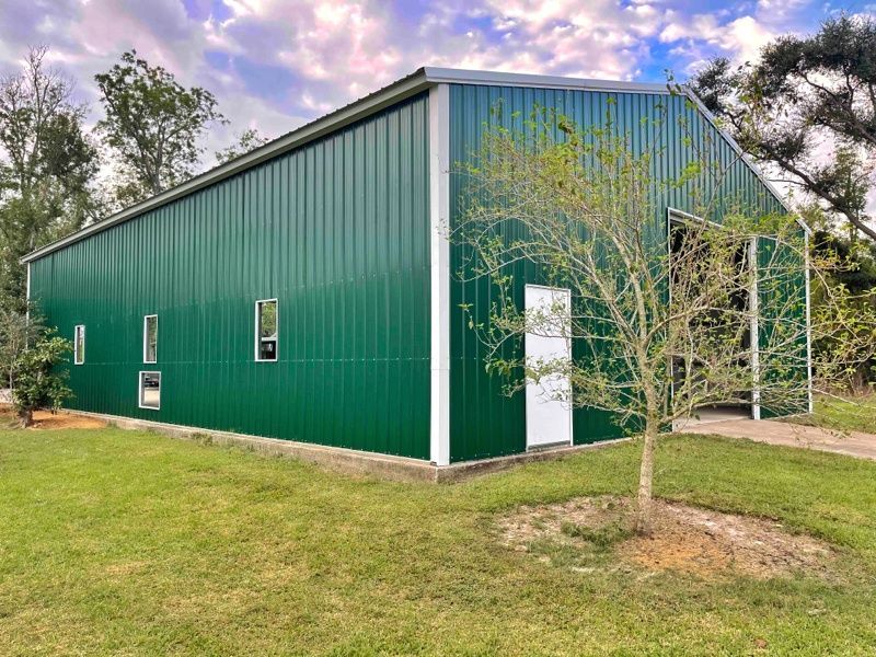 A green metal building with a white trim is sitting in the middle of a grassy field.