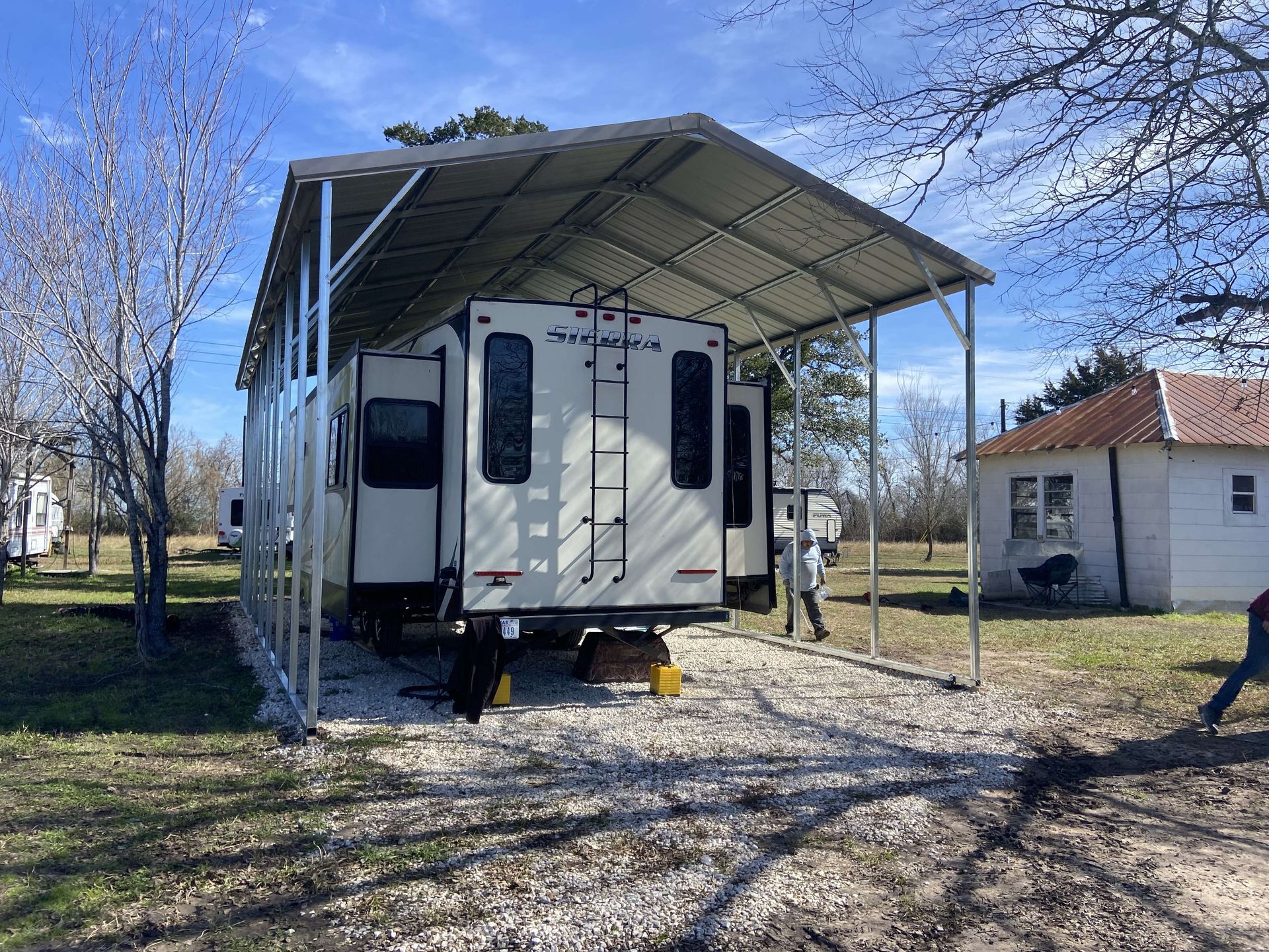 A rv is parked under a carport in a field.