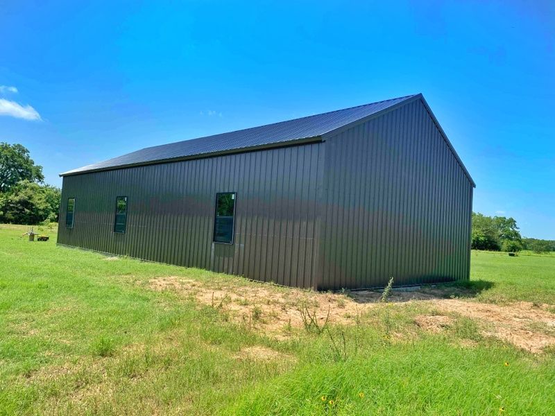 A large metal barn is sitting in the middle of a grassy field.
