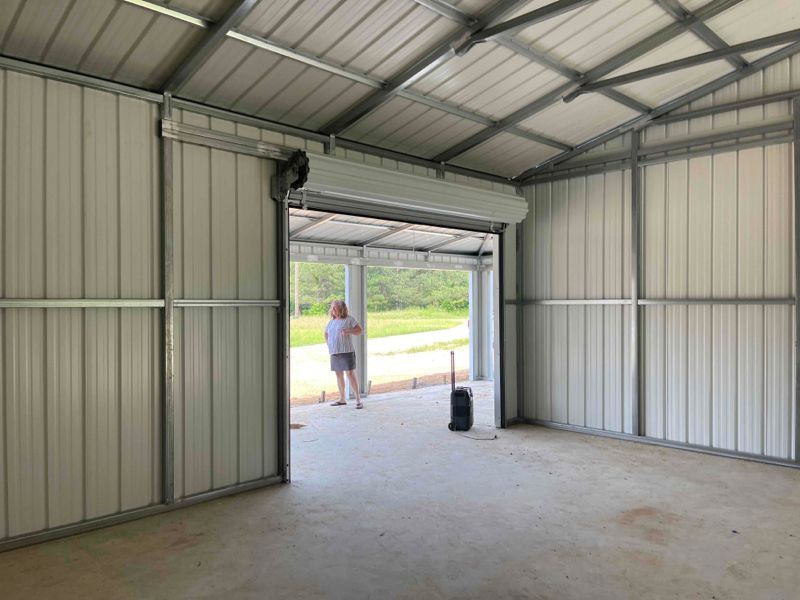 A woman is standing in a garage with a garage door open.