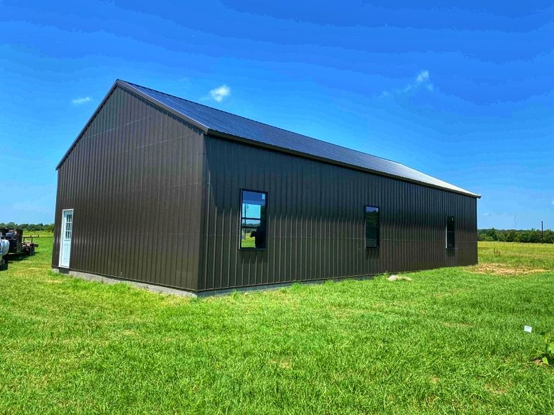 A large metal building is sitting in the middle of a grassy field.