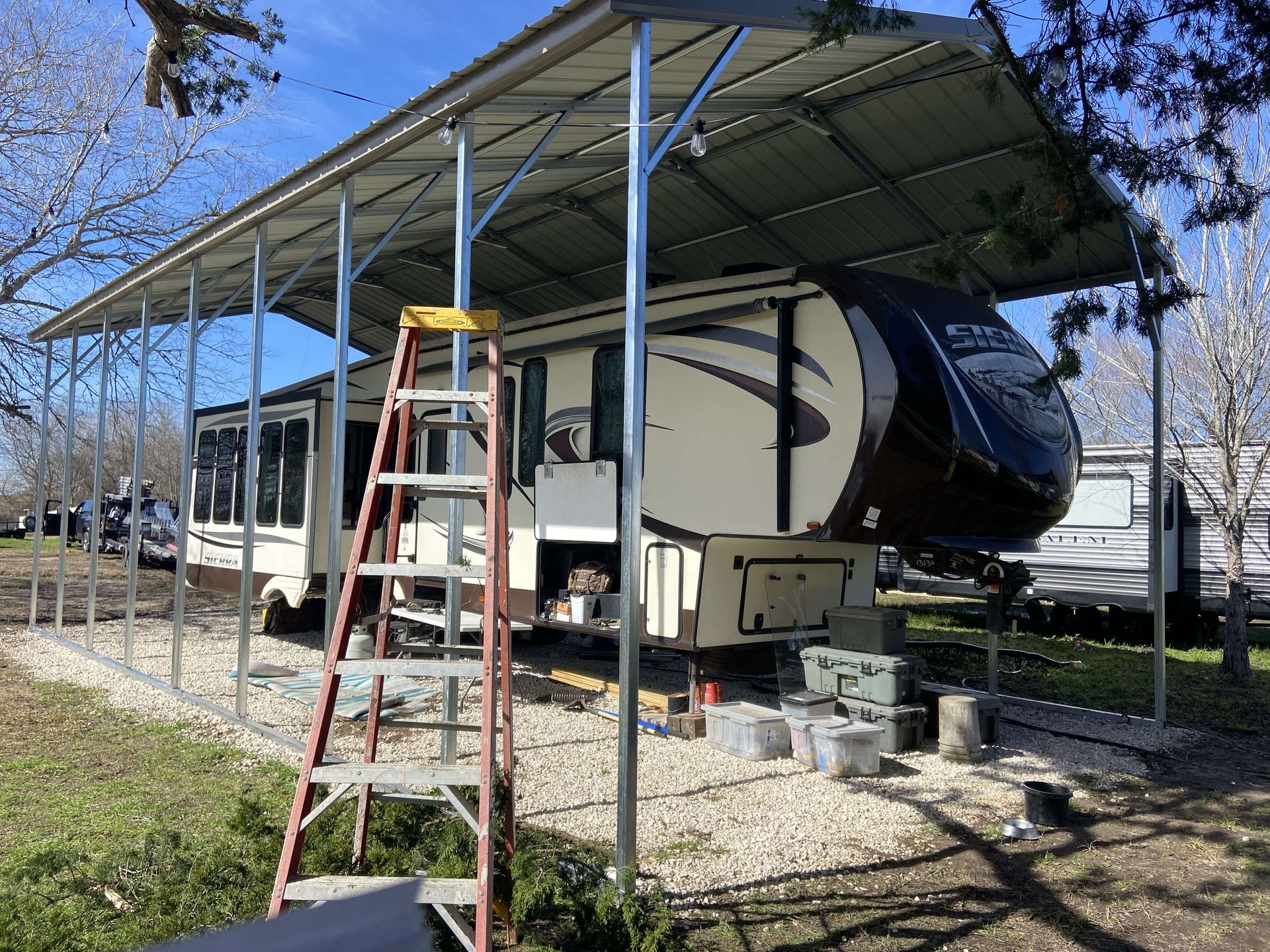 A ladder is sitting next to a trailer under a canopy.