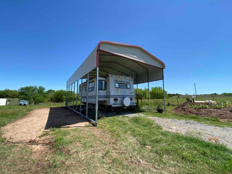 A rv is parked under a canopy in a field.