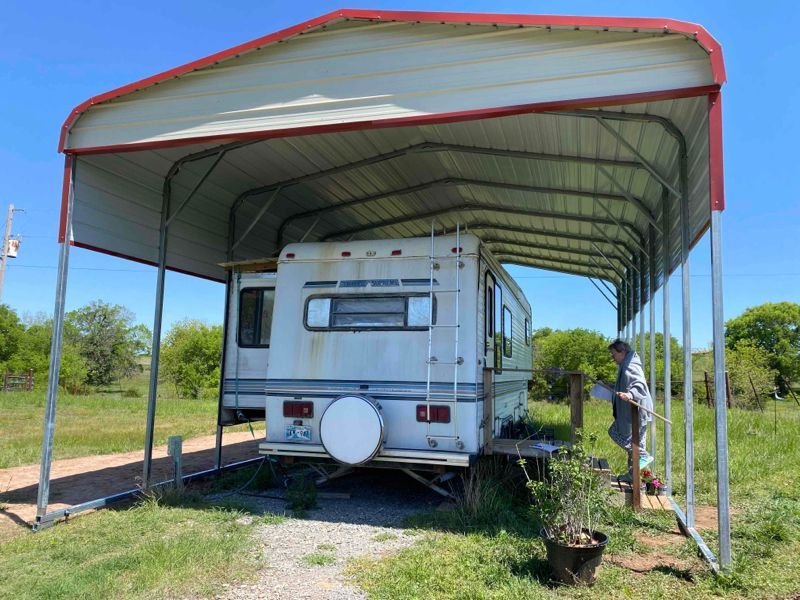 A white rv is parked under a canopy in a field.