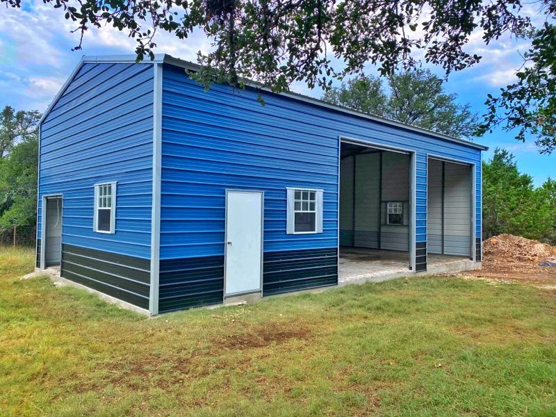 A blue and black garage with a white door is sitting in the middle of a grassy field.