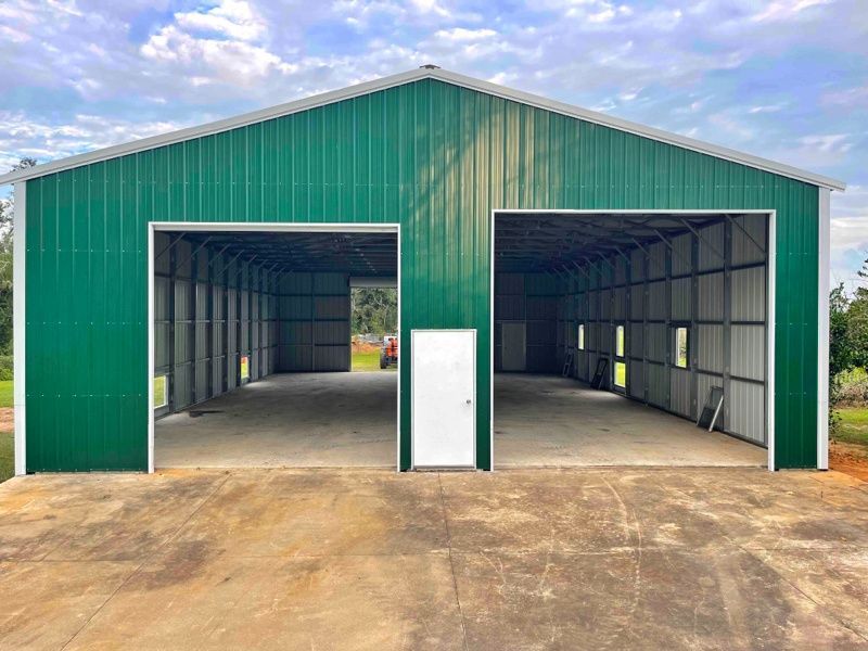 A green metal building with two garage doors and a white door.