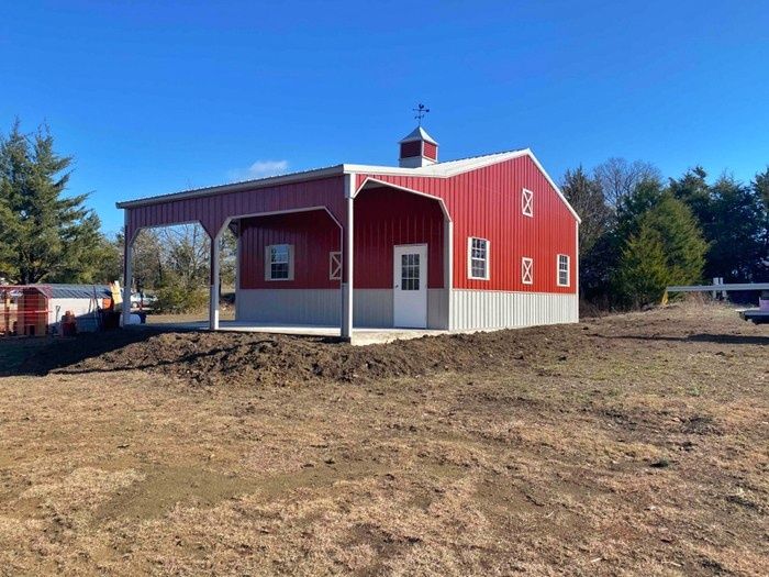 A red and white barn is sitting in the middle of a dirt field.