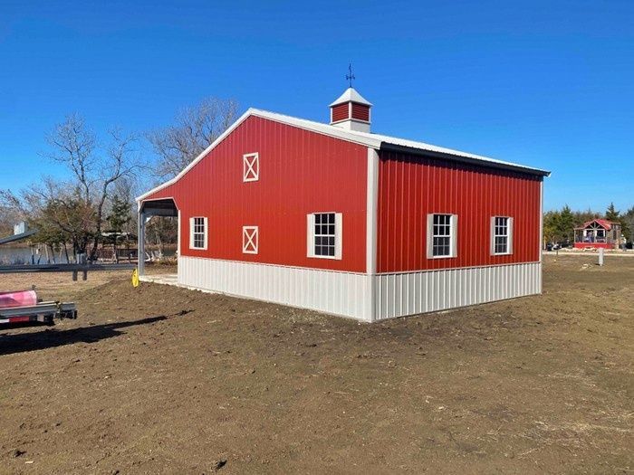 A red and white barn is sitting in the middle of a dirt field.
