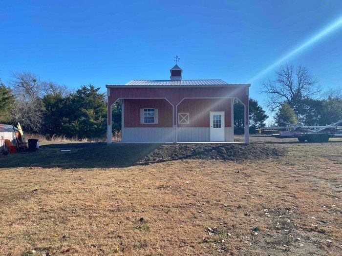 A red and white barn is sitting in the middle of a field.