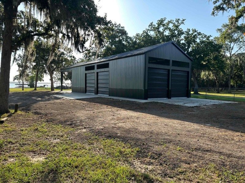 A large metal garage is sitting in the middle of a grassy field.