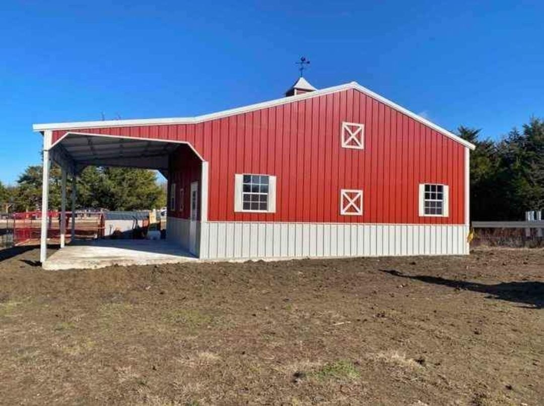 A red and white barn is sitting in the middle of a dirt field.