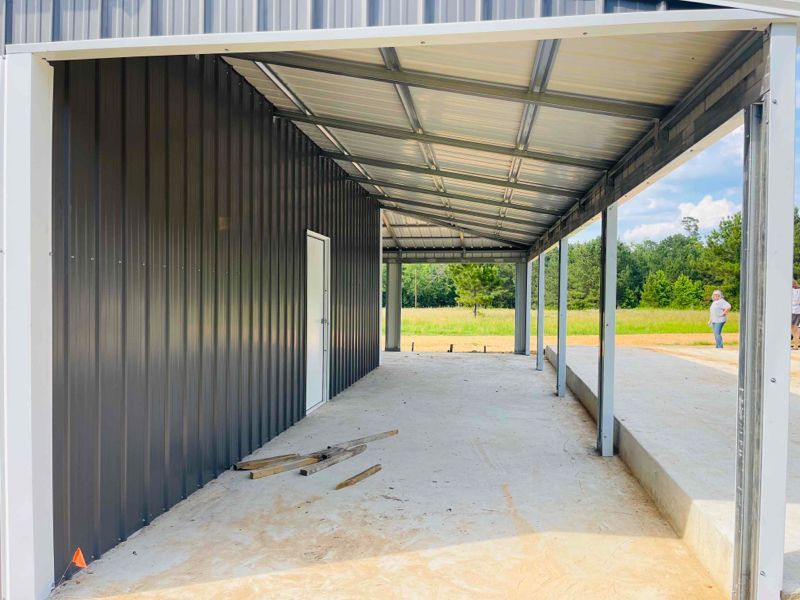 A large metal building with a covered porch and a concrete floor.