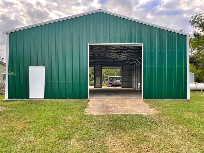 A green metal building with a white door is sitting in the middle of a grassy field.