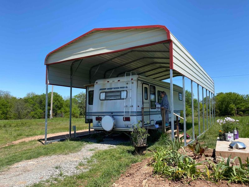 A rv is parked under a carport in a field.