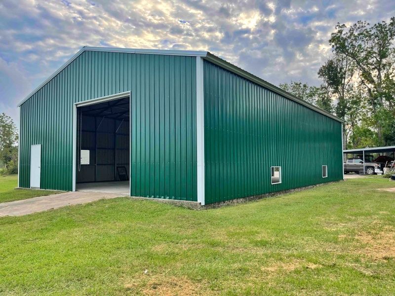 A large green metal building is sitting in the middle of a grassy field.