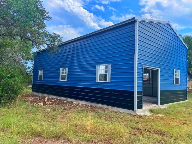 A blue and black building is sitting in the middle of a grassy field.