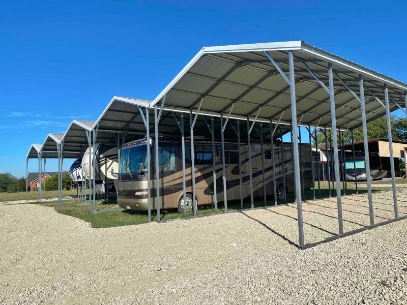 A row of rvs parked under a canopy in a gravel lot.