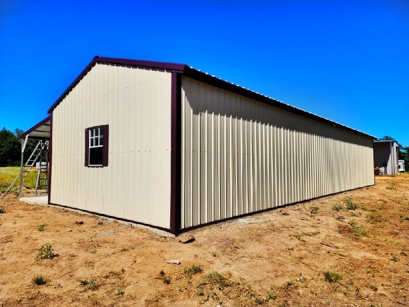 A large white building with a window on the side is sitting in the middle of a dirt field.