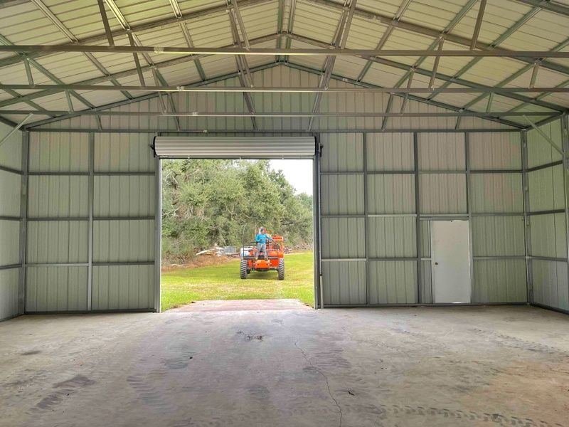 A man is driving a tractor in a garage with the door open.