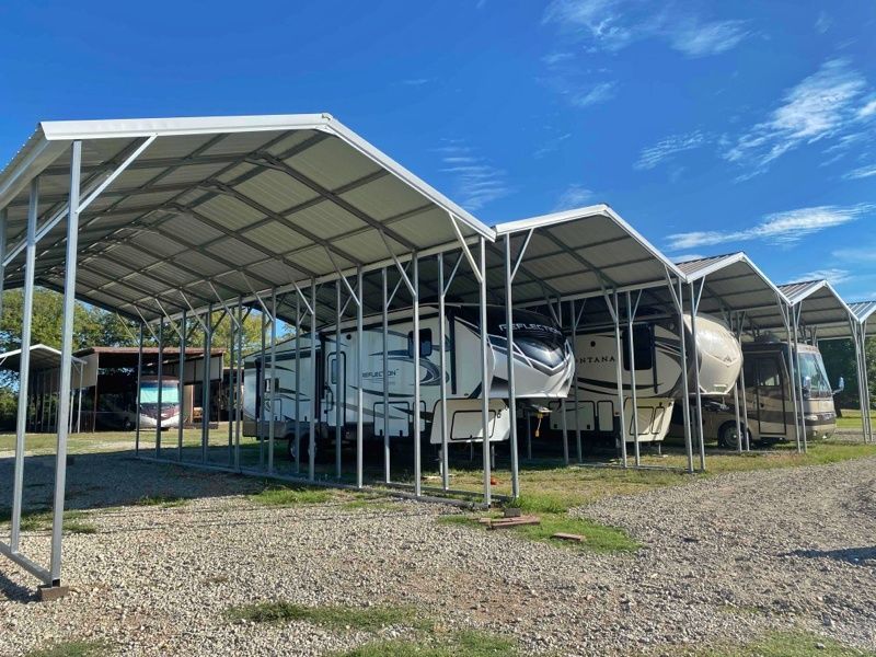 A row of rvs parked under a canopy in a gravel lot.