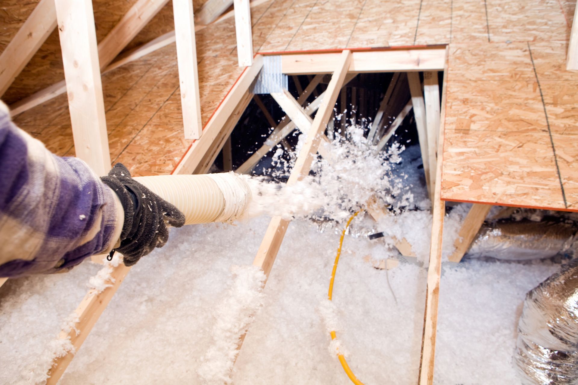 A person is blowing insulation into the attic of a house.