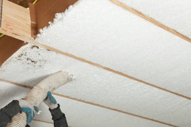 A person is blowing insulation into a ceiling with a vacuum.
