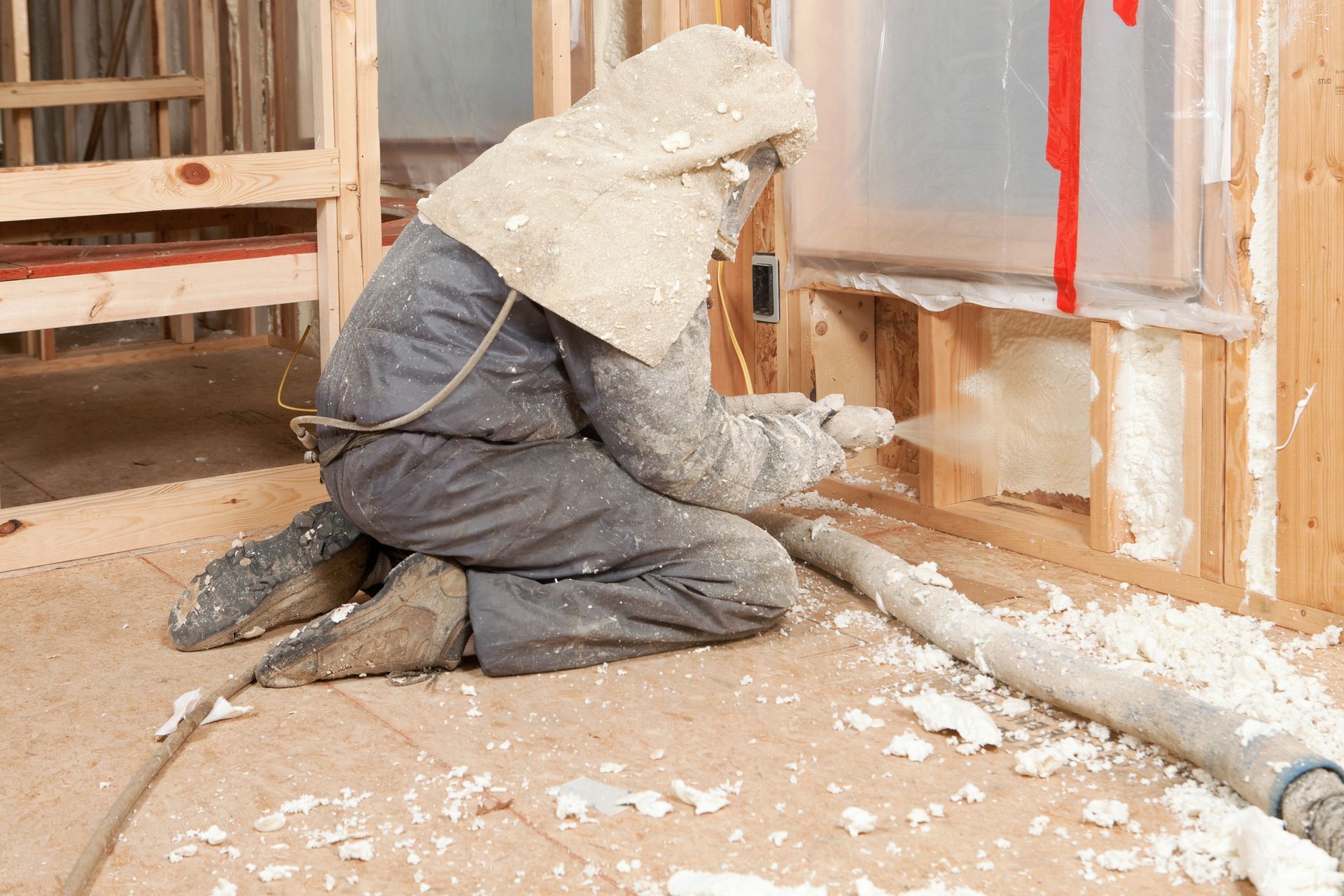 A man is spraying foam on a wall in a building under construction.