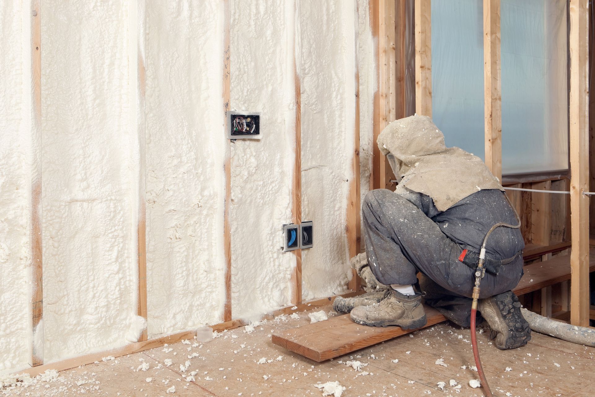 A man is spraying insulation on a wall in a room.