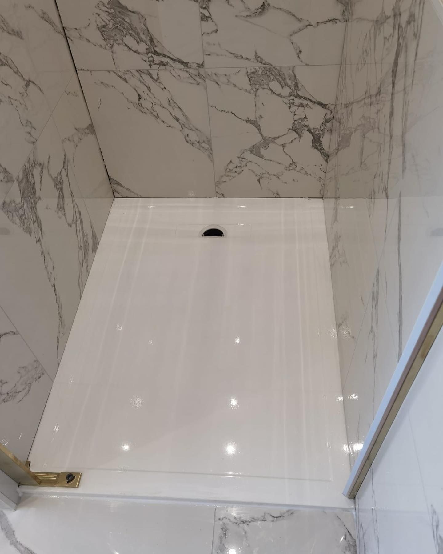 A white shower stall in a bathroom with marble walls.