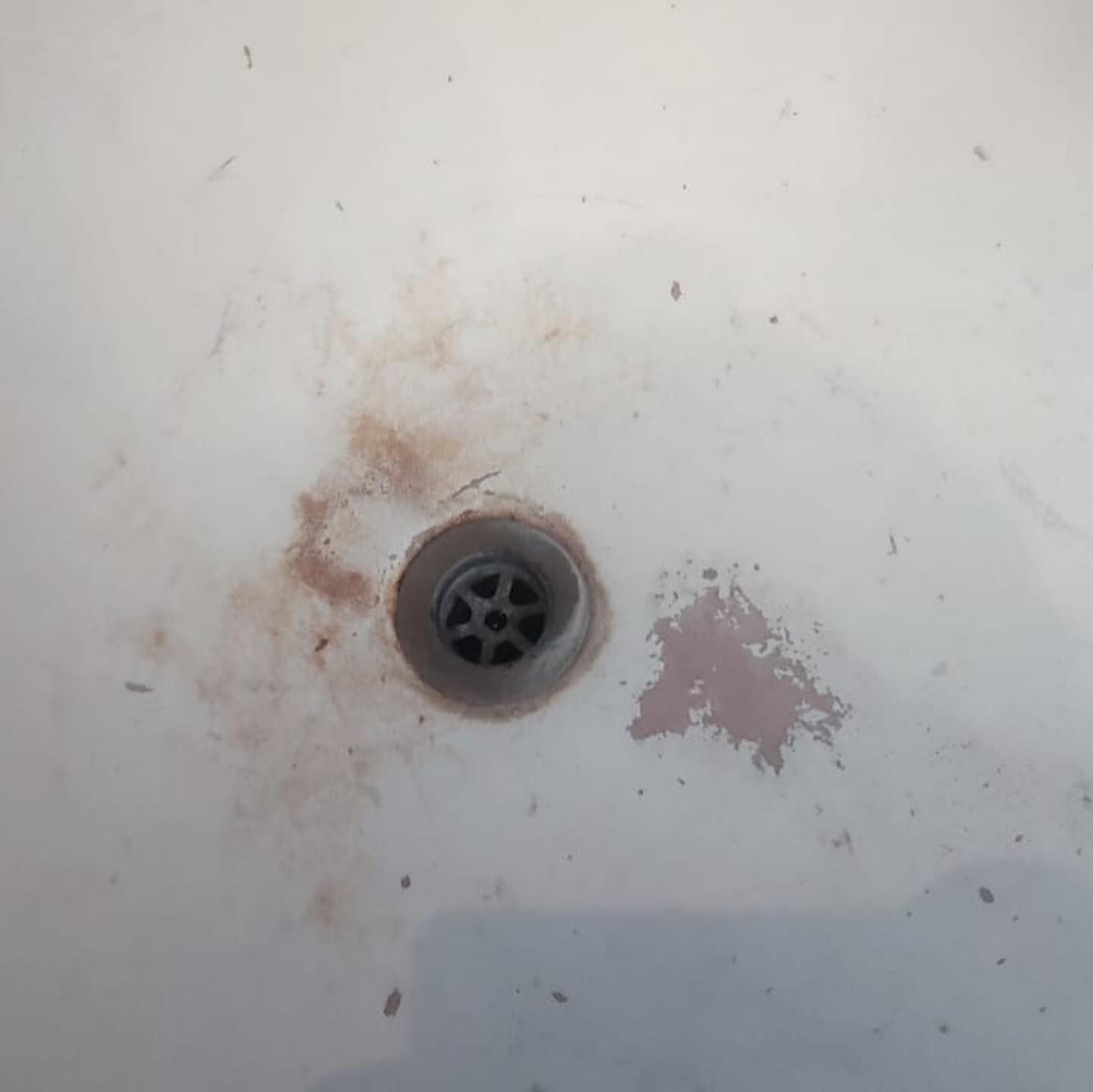 A close up of a dirty sink drain on a white surface.