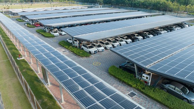 Solar panels covering a parking lot full of cars; grassy area in background.