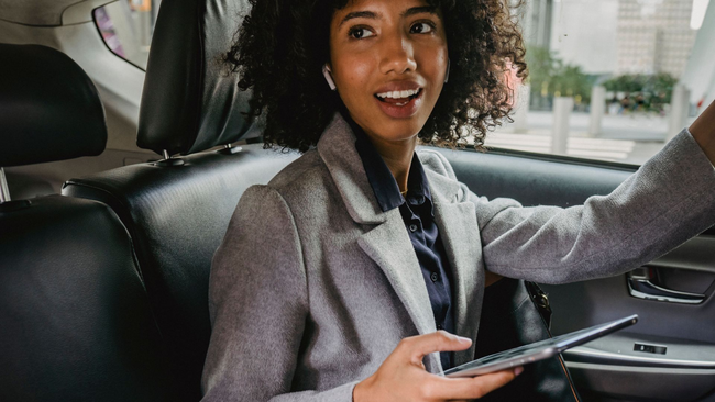 Woman in a car, talking on her phone, wearing a dark coat, looking concerned.
