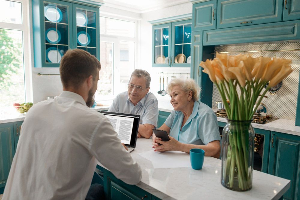 A Man Is Talking To An Elderly Couple In A Kitchen — Wegner Therapies In Pialba, QLD